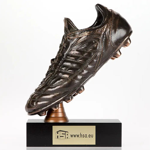 Echte voetbalschoen die verbronsd is en schuin op een zwart houten voet gemonteerd met voorbeeld van graveerplaatje met tekst.